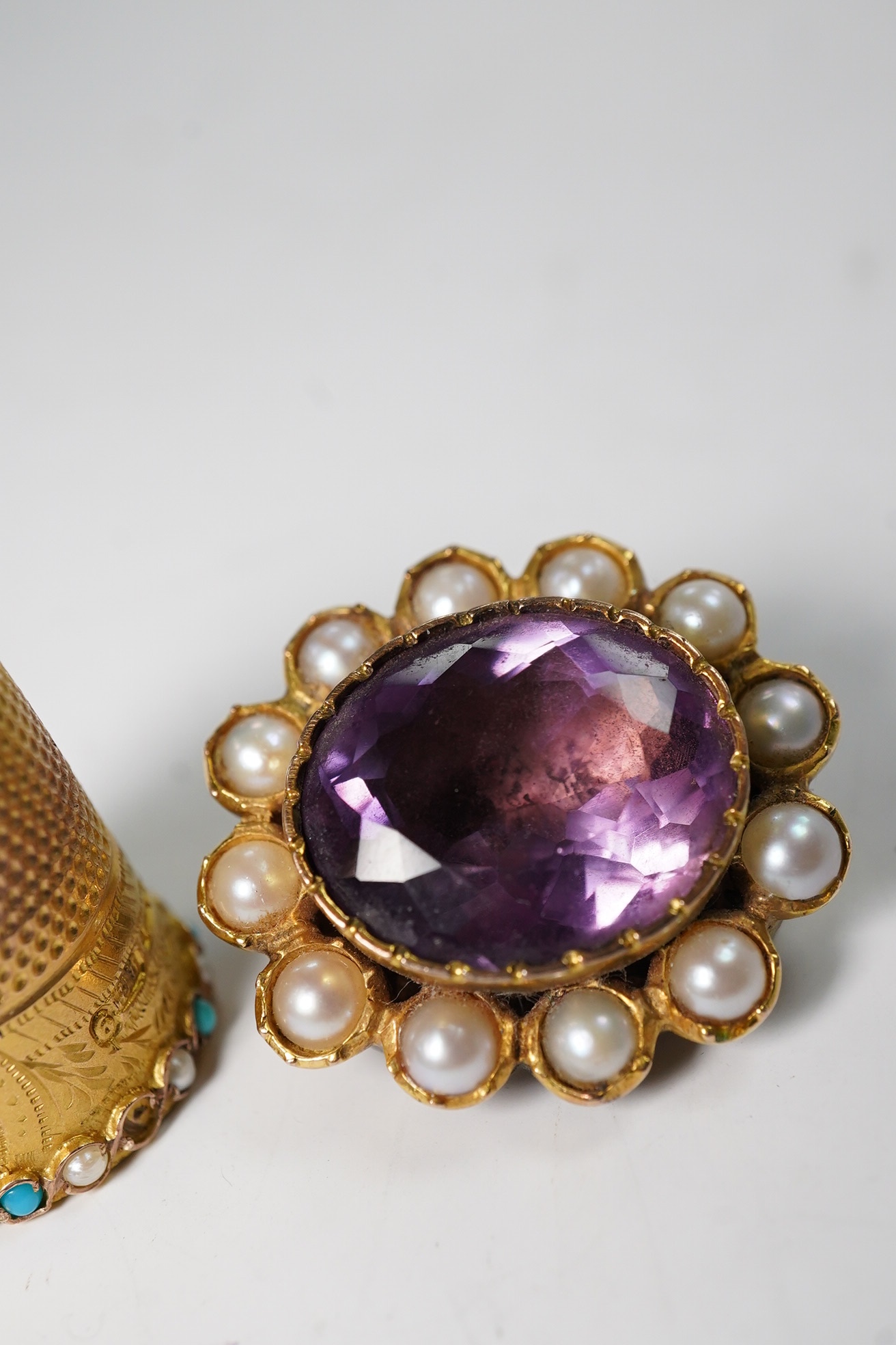A George V 9ct gold, turquoise and seed pearl set thimble, 5.9 grams, and an amethyst and split pearl set yellow metal clasp, converted to a brooch. Condition - poor to fair